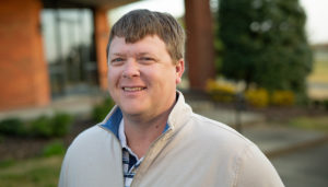 A man in a beige jacket standing outside.